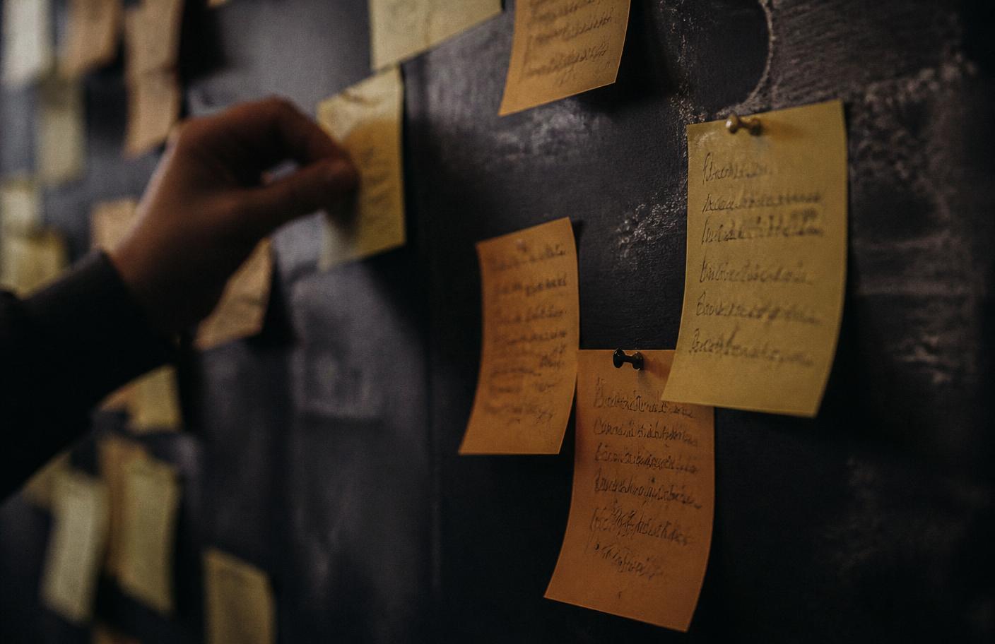 Handwritten amber sticky notes pinned to a dark wall, each one a founder's blocker